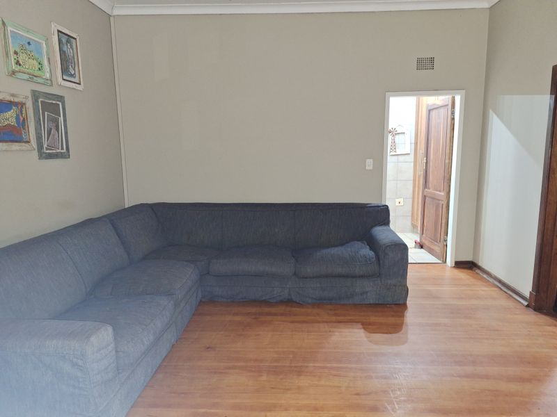 A living room featuring laminate flooring and neutral wall tones, with a doorway leading to an adjacent tiled area.