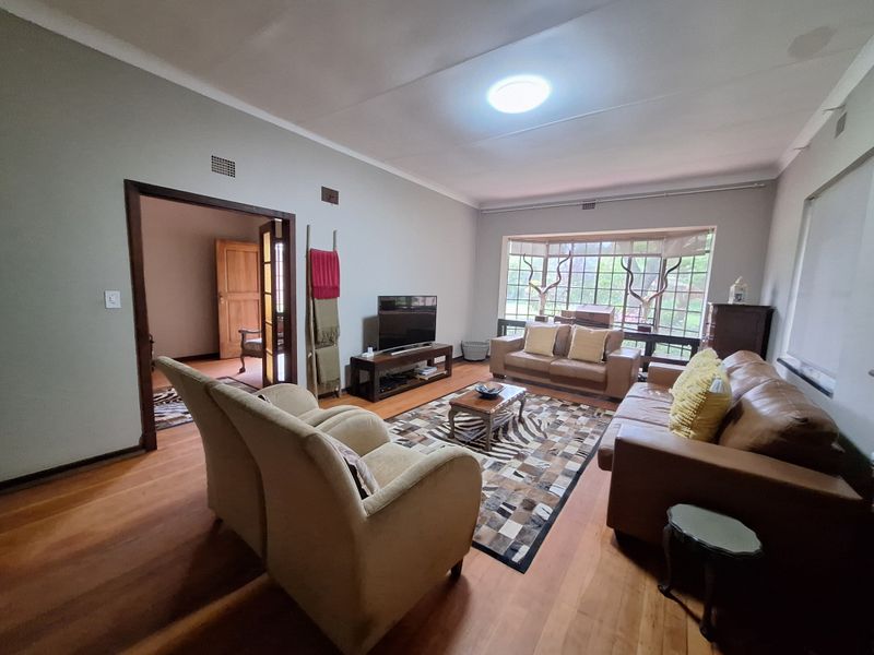 Spacious living room featuring warm hardwood flooring, a large bay window, and coved ceilings, offering a comfortable and inviting atmosphere.