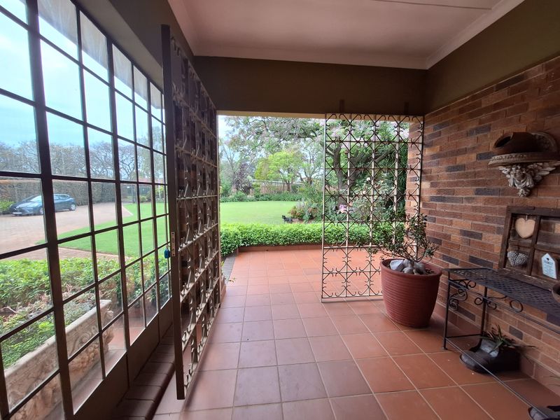 A covered patio area featuring terracotta floor tiles, exposed brick walls, and large glass windows overlooking the garden.