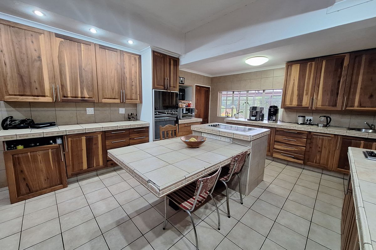 Spacious kitchen featuring extensive wooden cabinetry, tiled countertops, a central island with a built-in hob, and tiled flooring throughout.