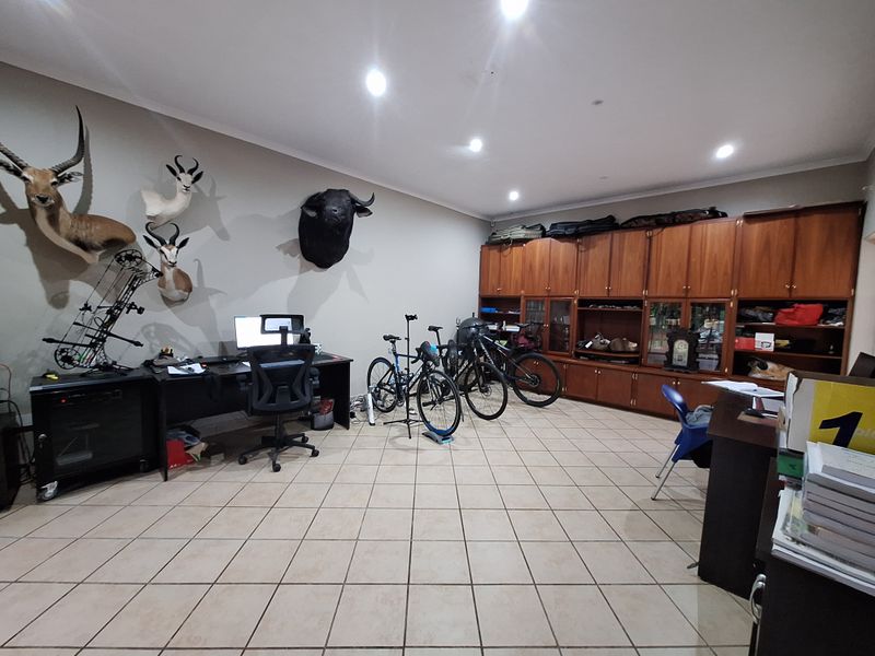 Spacious home office featuring extensive built-in wooden cabinetry, recessed downlighting, and durable tiled flooring, offering ample storage and workspace.