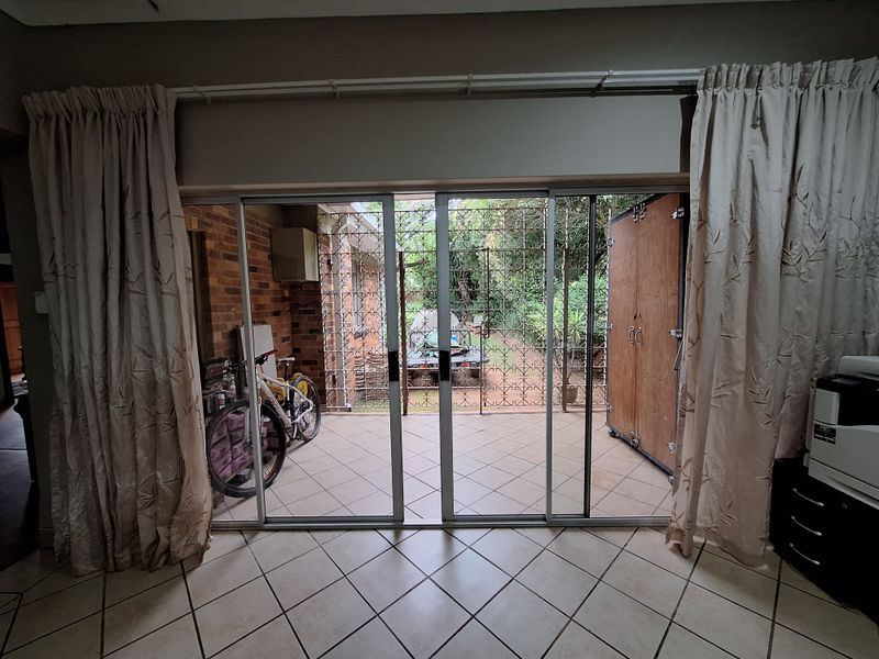A covered patio area featuring tiled flooring, exposed brickwork, and sliding glass doors with security gates leading to the garden.