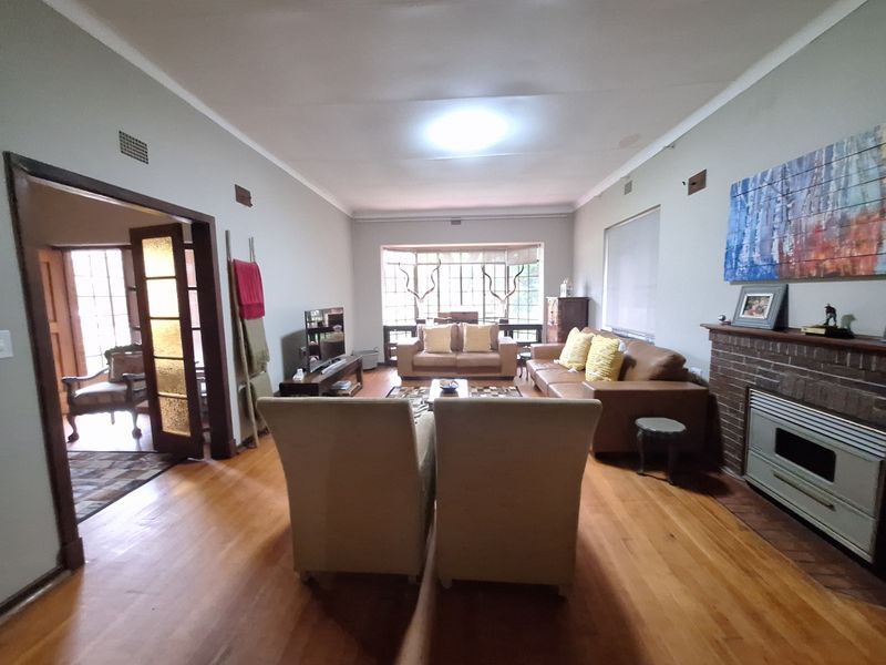 Spacious living room featuring polished hardwood floors, a brick fireplace with a built-in gas heater, and large bay windows providing natural light.