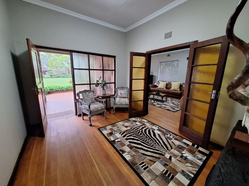 A bright living area featuring polished hardwood flooring, elegant crown molding, and classic timber-framed french doors providing direct access to the outdoor patio.