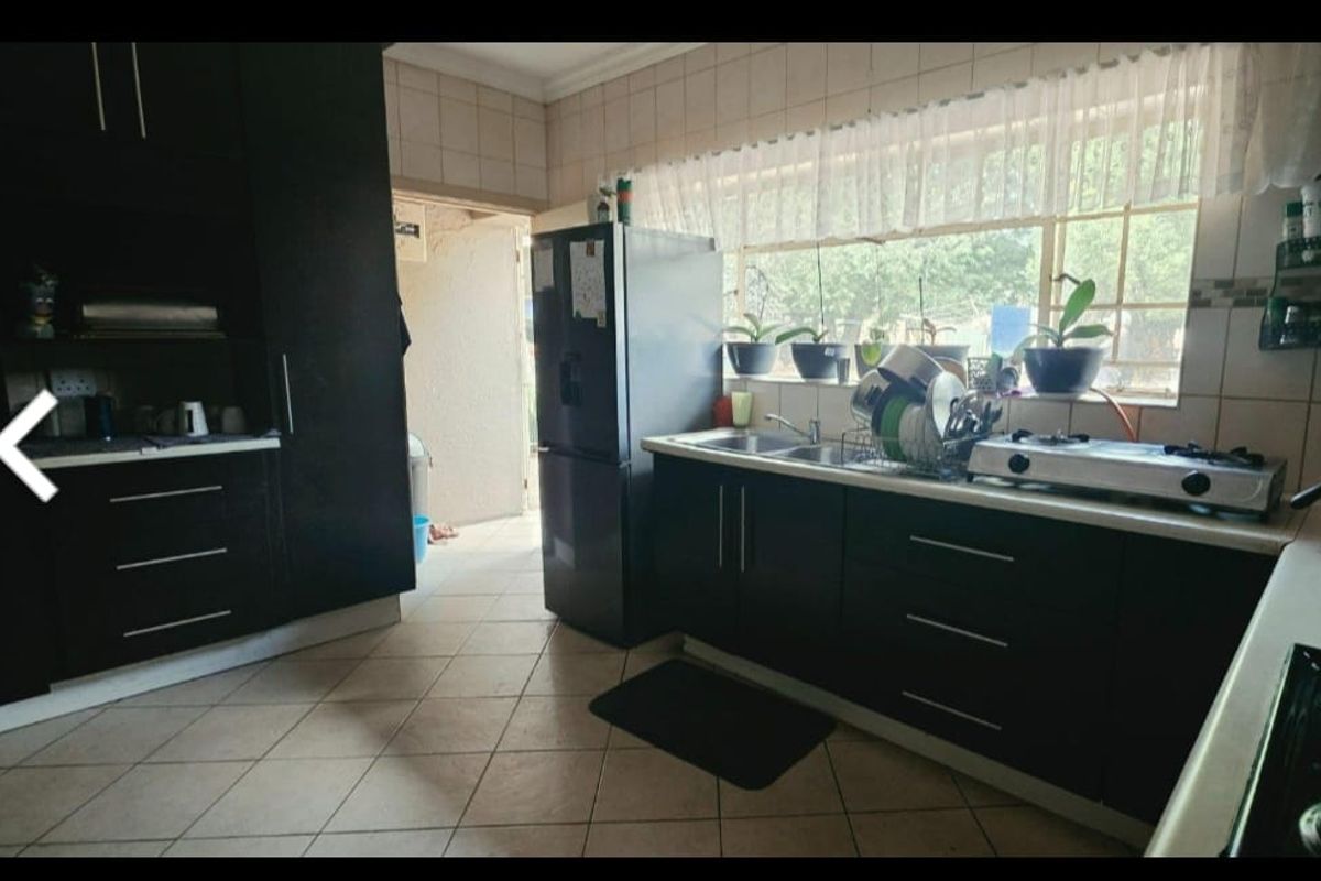 A functional kitchen featuring dark built-in cabinetry, a double sink, gas hob, and tiled finishes, offering a practical layout with natural light.