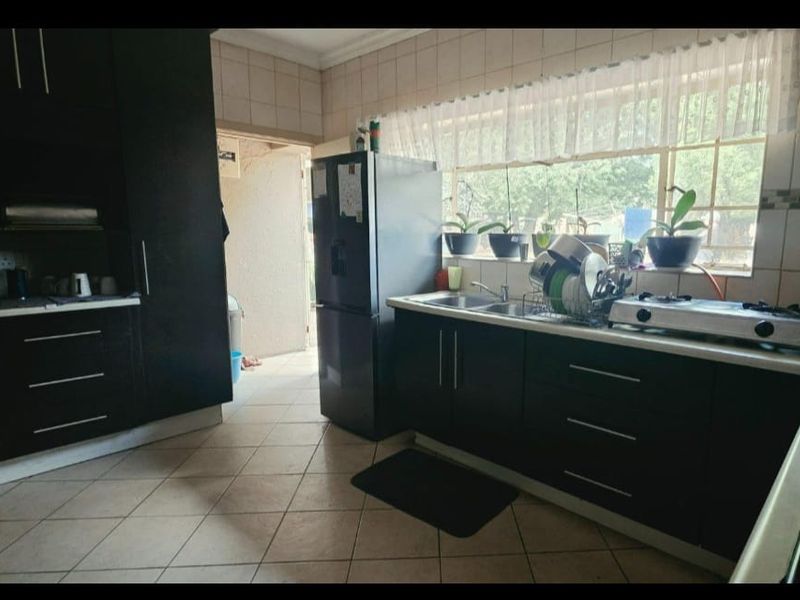 A functional kitchen featuring dark built-in cabinetry, a double sink, gas hob, and tiled finishes, offering a practical layout with natural light.