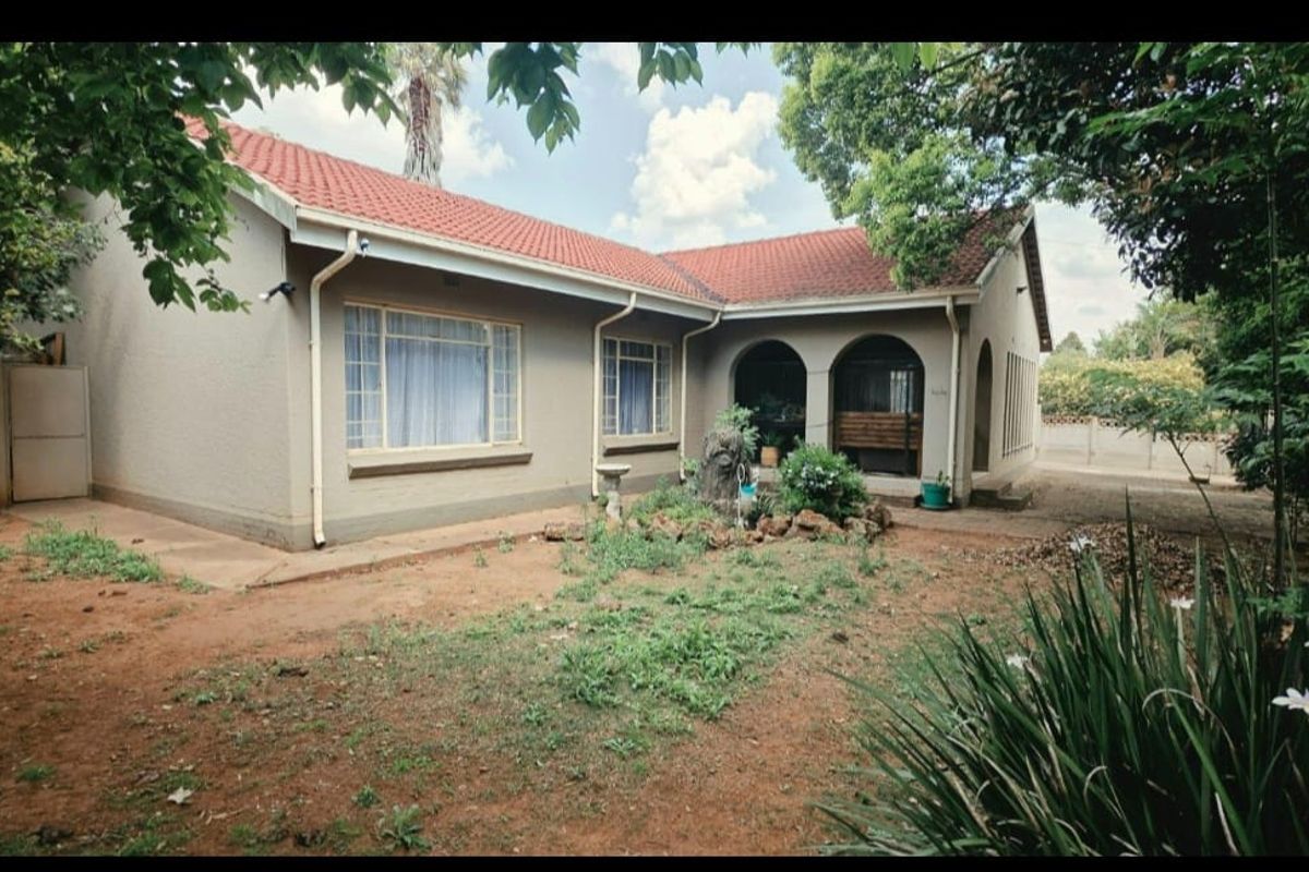 Rear view of a single-story house featuring a terracotta tiled roof, plastered walls, and an arched patio area overlooking a garden.