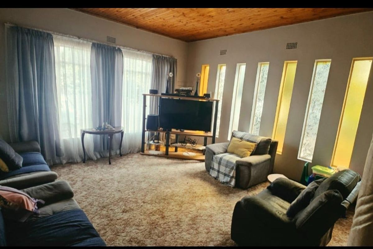 A living room featuring a timber ceiling, large windows, and unique vertical accent windows, currently finished with dated carpeting.