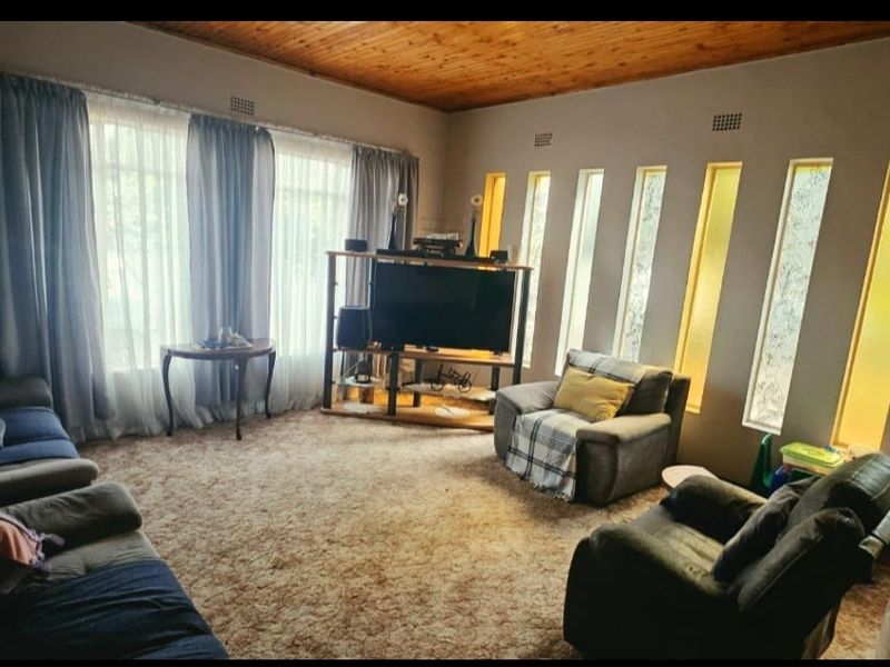 A living room featuring a timber ceiling, large windows, and unique vertical accent windows, currently finished with dated carpeting.