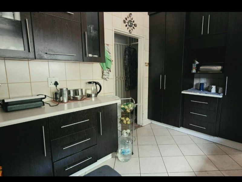 A functional kitchen featuring dark wood cabinetry, tiled backsplash, and tiled flooring with ample storage space.