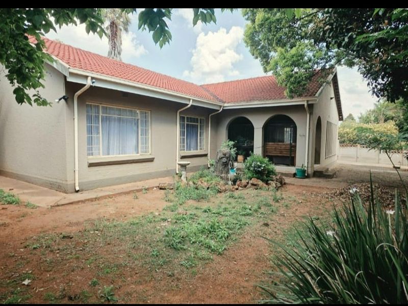 Rear view of a single-story house featuring a tiled roof, plastered exterior walls, and a covered arched patio area overlooking a garden.