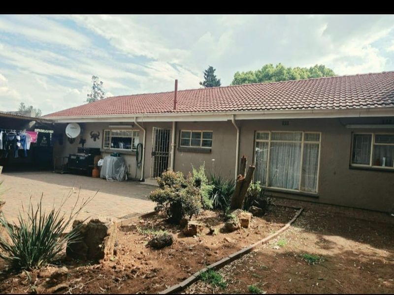 Rear view of the house featuring a tiled roof, paved patio area, and established garden space with security features on windows and doors.