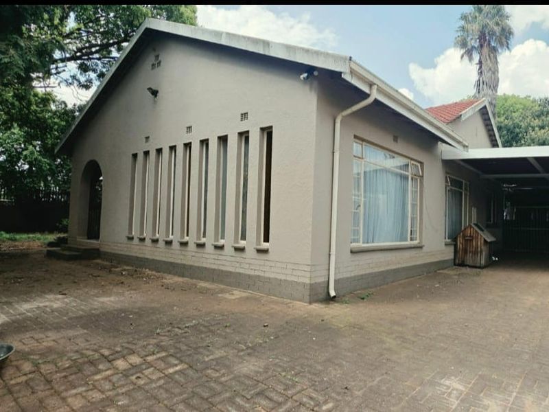 Side view of a residential house featuring a paved driveway, carport, and distinctive vertical window design with plastered exterior walls.