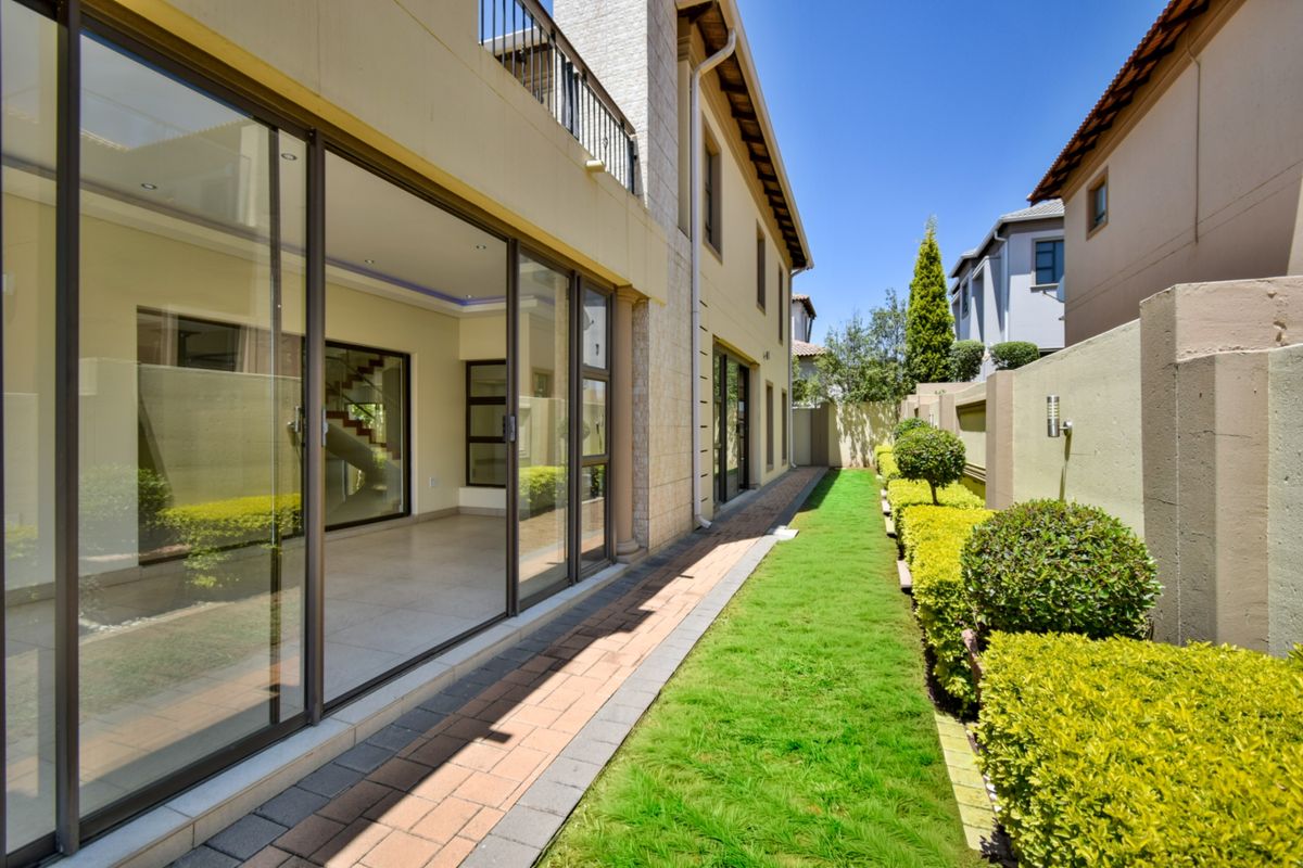 A well-maintained rear exterior view featuring a paved walkway, manicured lawn, landscaped hedges, and large sliding glass doors leading into the home.