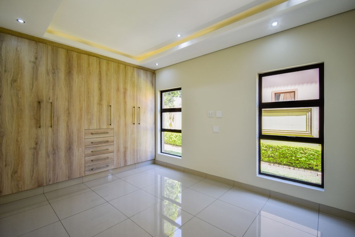 A bright, modern bedroom featuring polished tile flooring, recessed ceiling lighting, and extensive built-in wooden cabinetry with ample storage space.
