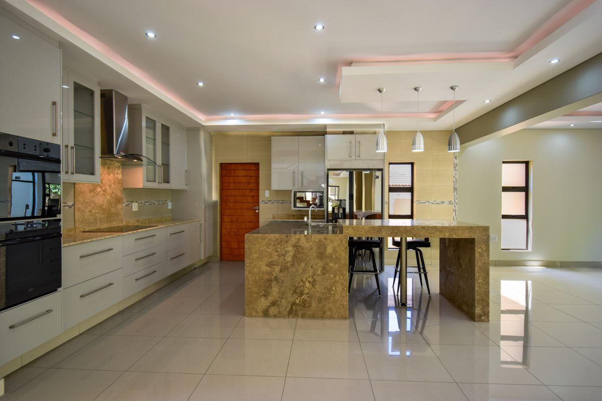 Modern open-plan kitchen featuring stone-topped island, built-in oven, extractor fan, and sleek cabinetry with recessed ceiling lighting.