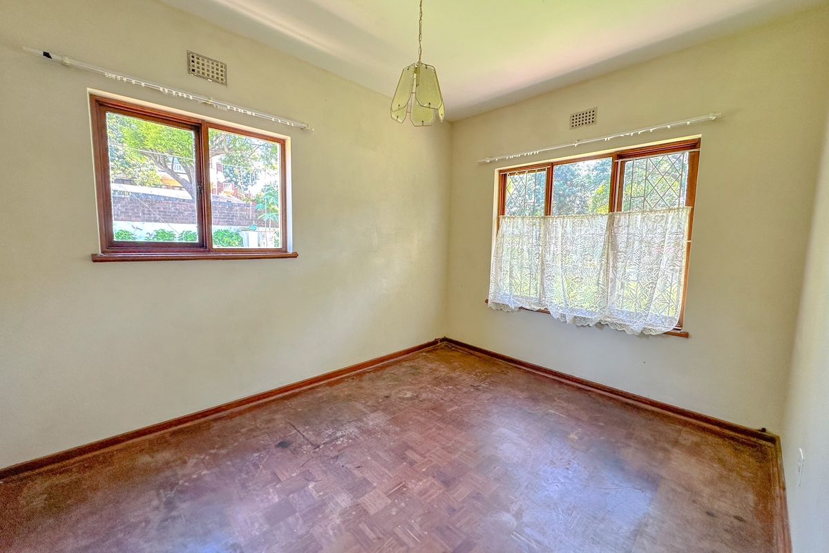 An empty bedroom featuring original parquet flooring, timber-framed windows, and neutral wall finishes, offering a blank canvas for renovation.