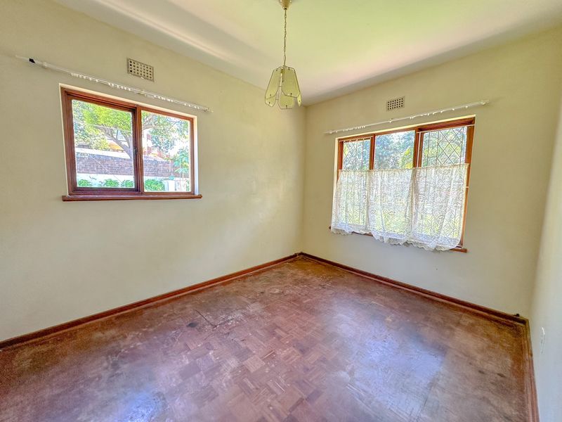 An empty bedroom featuring original parquet flooring, timber-framed windows, and neutral wall finishes, offering a blank canvas for renovation.
