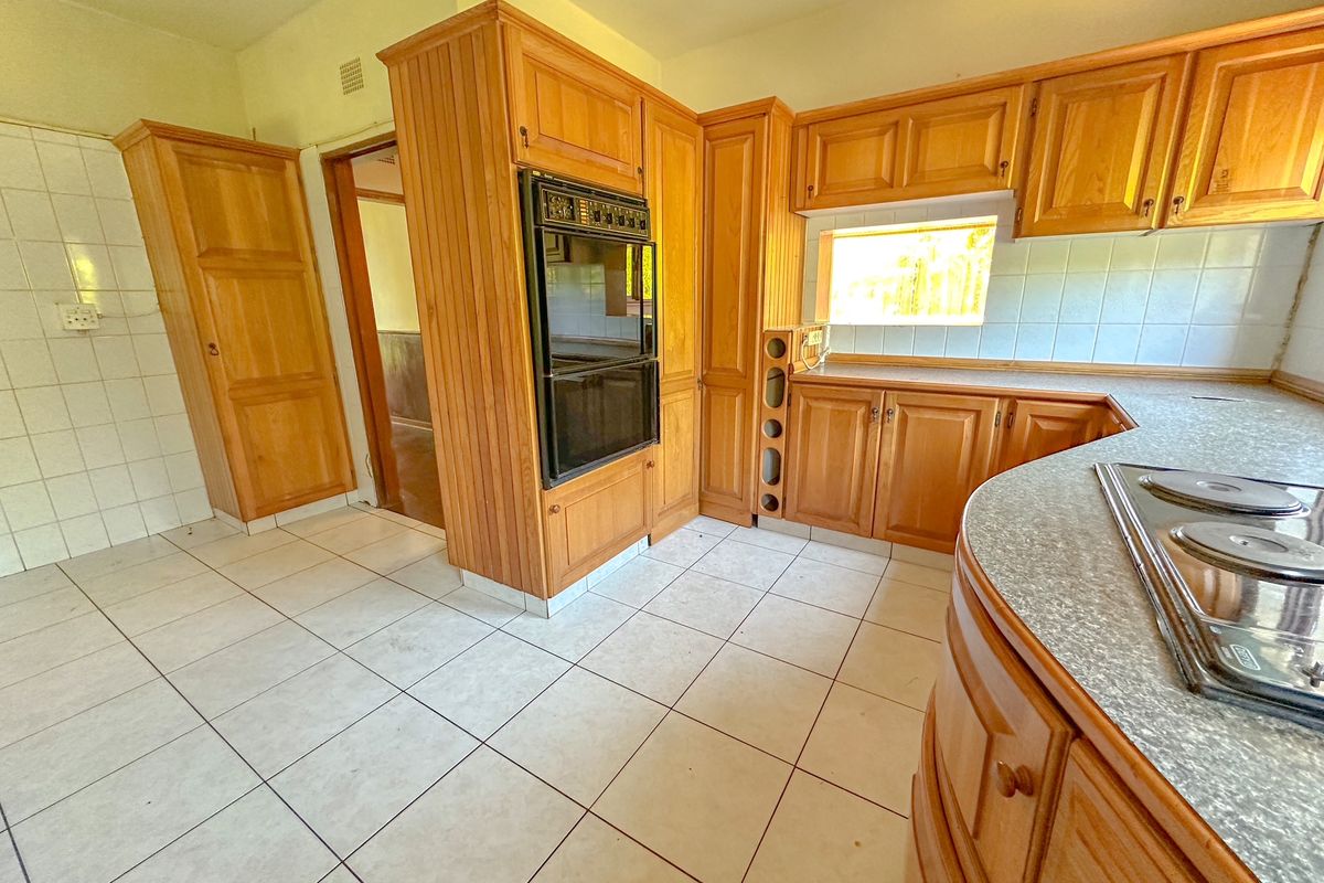 A functional kitchen featuring traditional wooden cabinetry, a built-in double oven, electric hob, and tiled flooring, offering a classic layout ready for modernization.