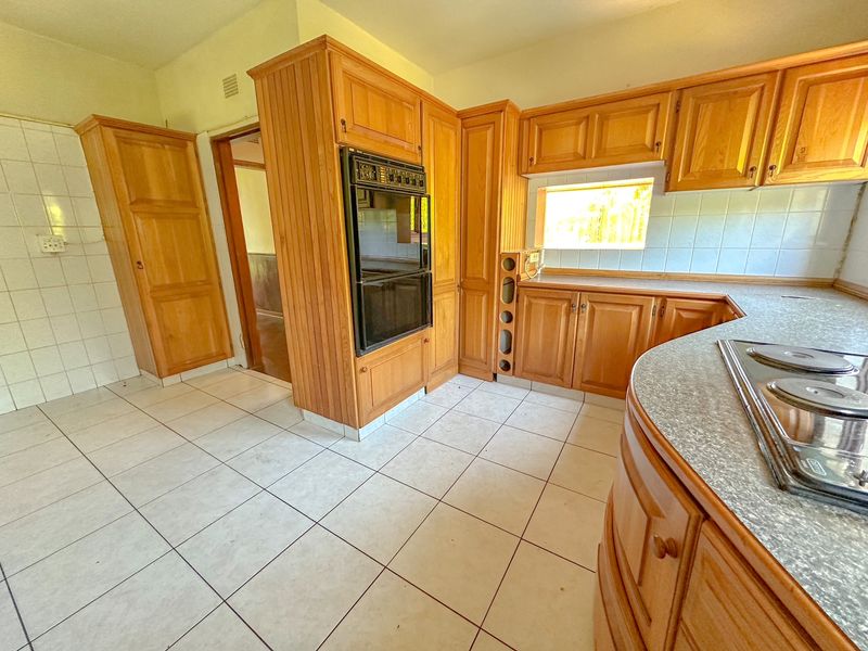 A functional kitchen featuring traditional wooden cabinetry, a built-in double oven, electric hob, and tiled flooring, offering a classic layout ready for modernization.