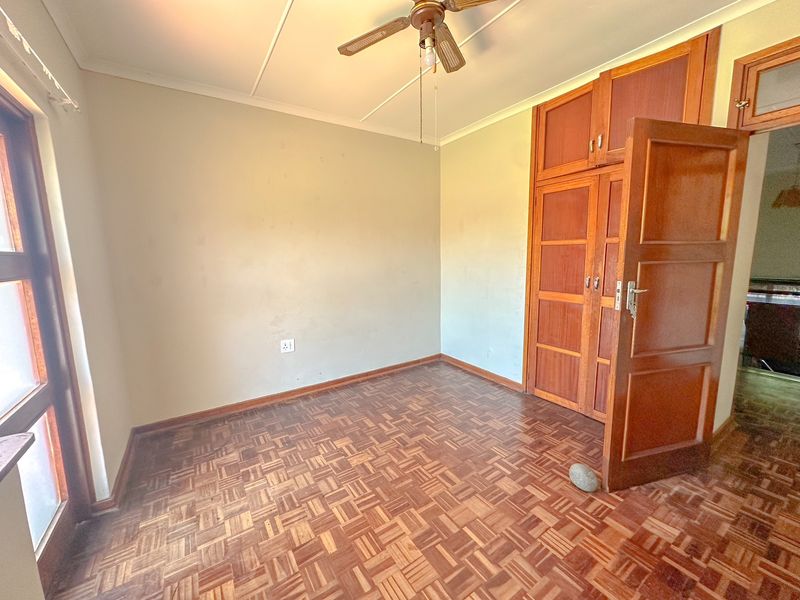 A vacant bedroom featuring classic parquet flooring, built-in wooden cabinetry, and a ceiling fan, offering a blank canvas for personalization.