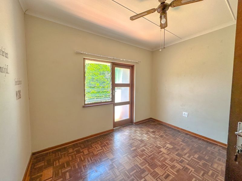 A vacant bedroom featuring classic parquet flooring, a ceiling fan, and a louver window with an integrated timber door.