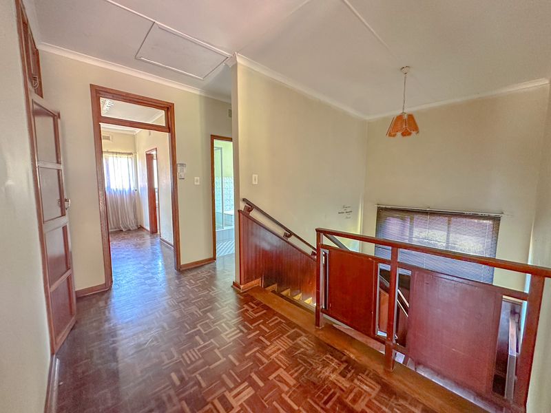 Spacious upper-level hallway featuring classic parquet flooring, a wooden staircase with a matching balustrade, and access to multiple rooms.