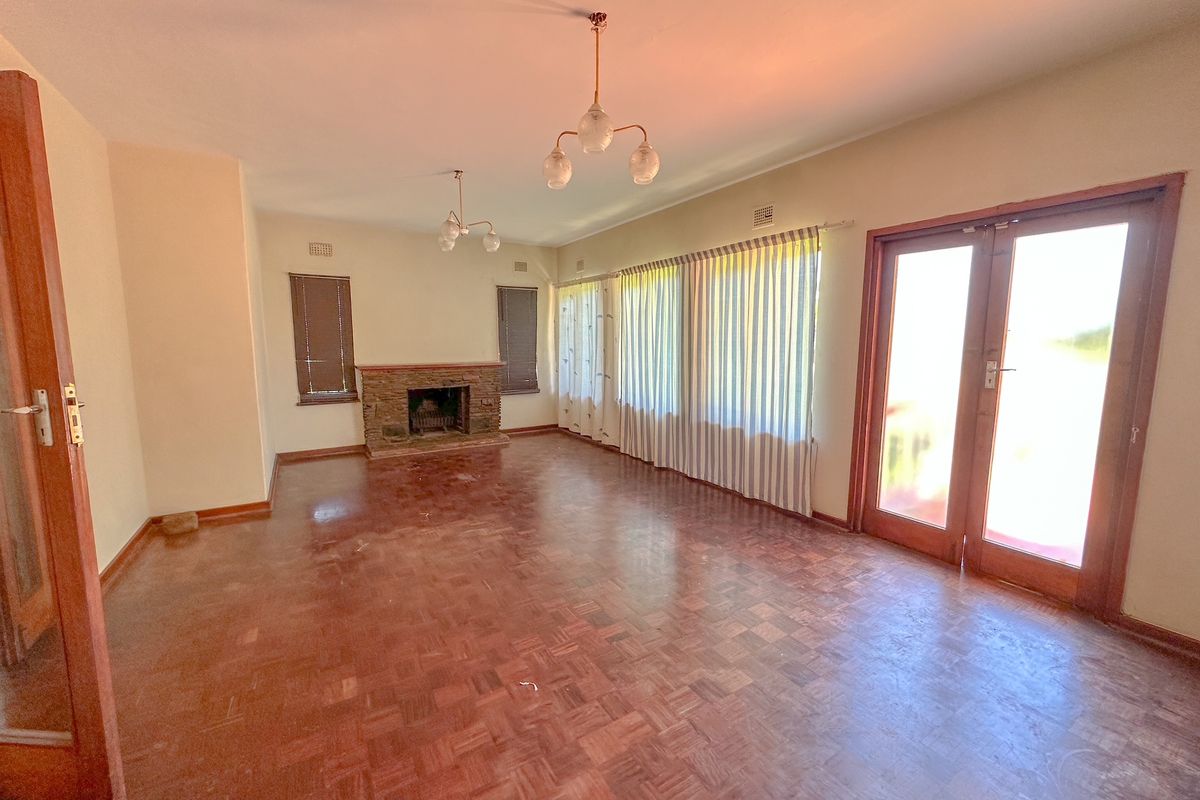 Spacious living room featuring original parquet flooring, a stone fireplace, and double doors leading to the exterior, offering a bright and versatile living space.