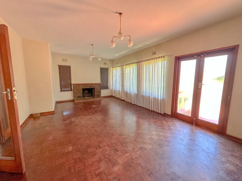 Spacious living room featuring original parquet flooring, a stone fireplace, and double doors leading to the exterior, offering a bright and versatile living space.