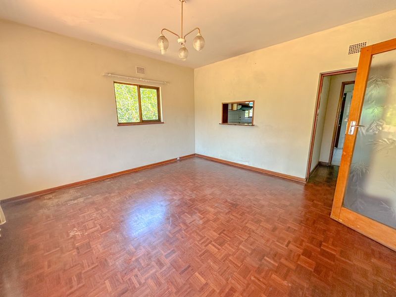 An empty living room featuring original parquet flooring, a serving hatch to the kitchen, and a timber door, offering a blank canvas for renovation.