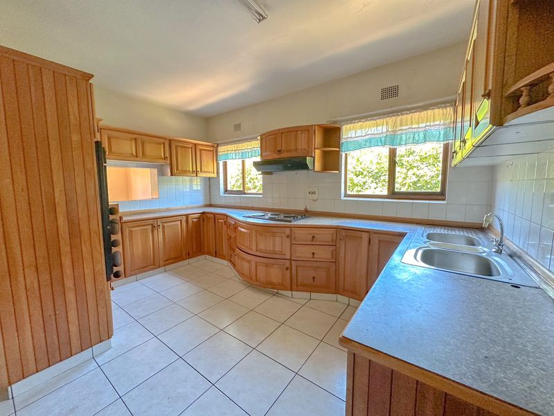 A spacious kitchen featuring traditional wooden cabinetry, laminate countertops, a double bowl sink, and a built-in hob with an extractor fan.