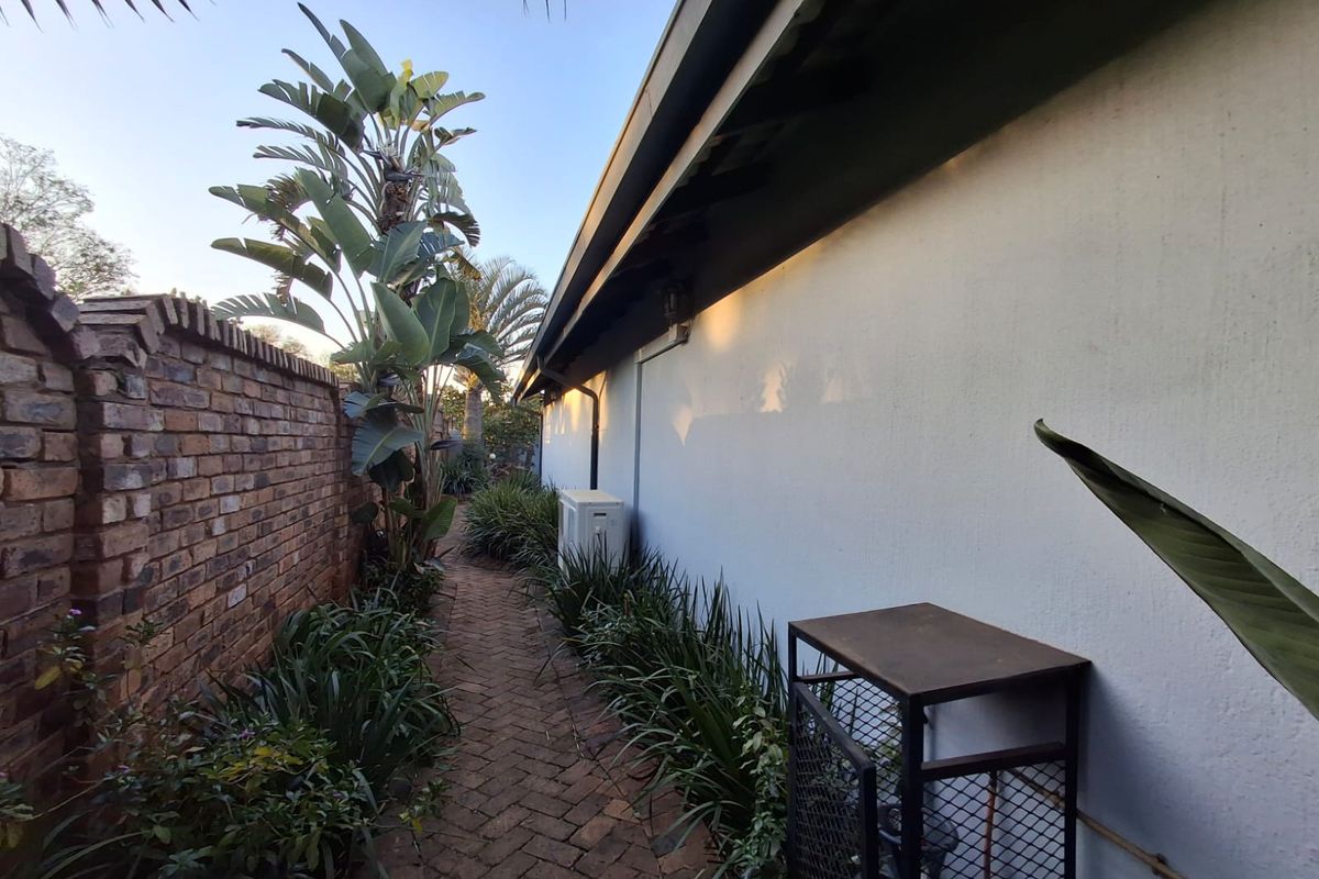 A side exterior pathway featuring a brick paved walkway, a brick boundary wall, and established garden landscaping along the side of the house.