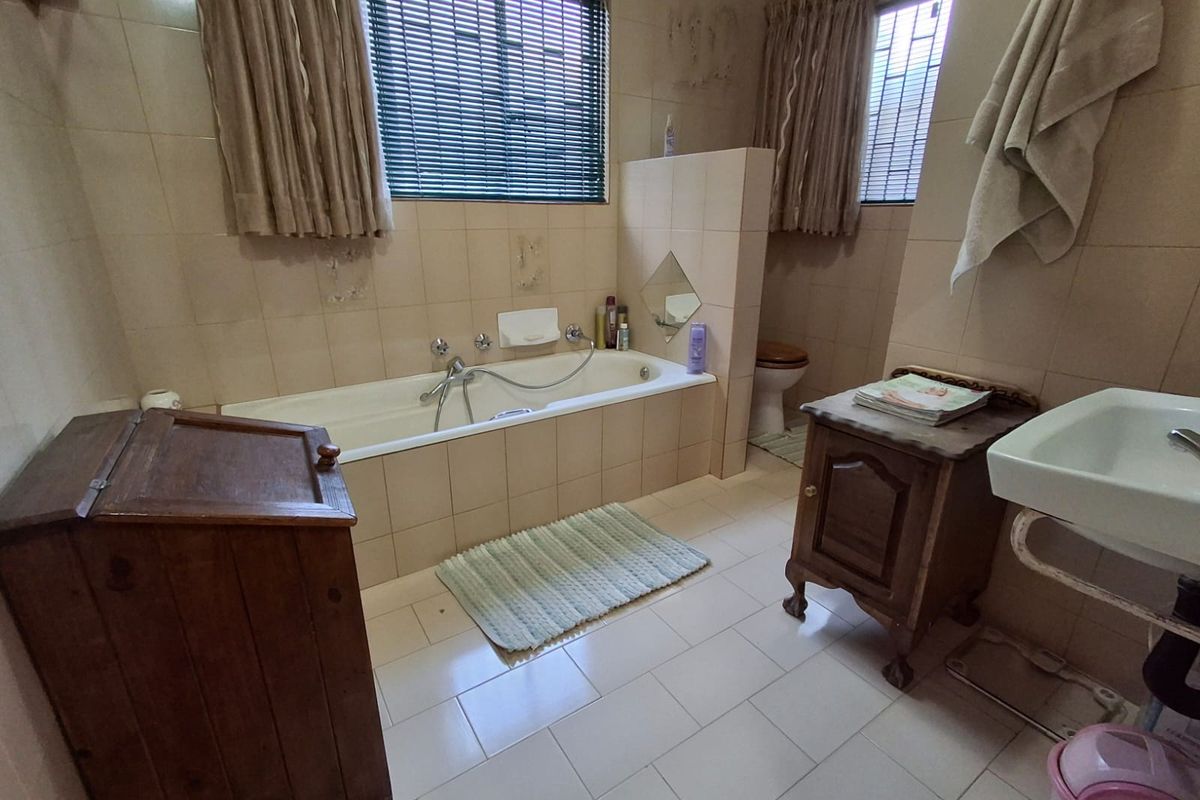 A dated bathroom featuring a built-in bathtub, wall-mounted basin, and toilet, with neutral wall and floor tiling throughout.