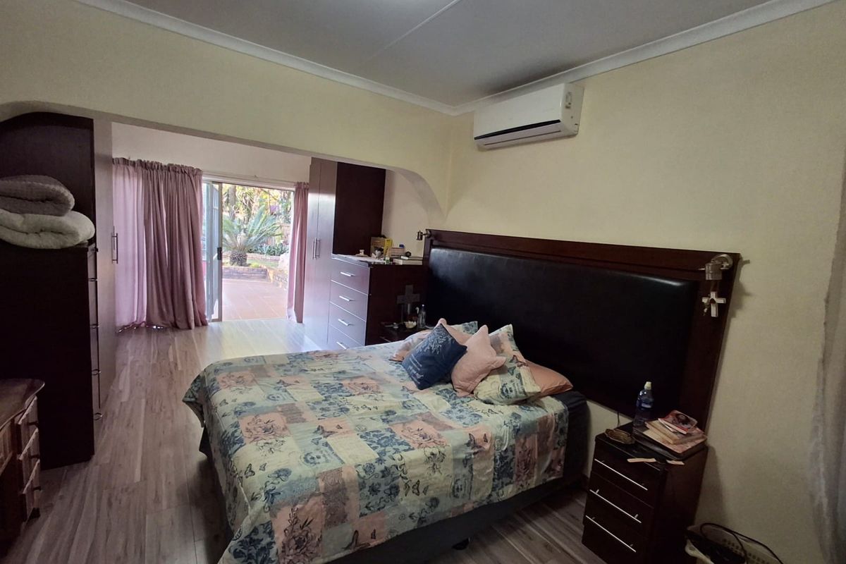 Spacious bedroom featuring laminate flooring, built-in cupboards, a wall-mounted air conditioner, and direct access to an outdoor patio area through sliding glass doors.