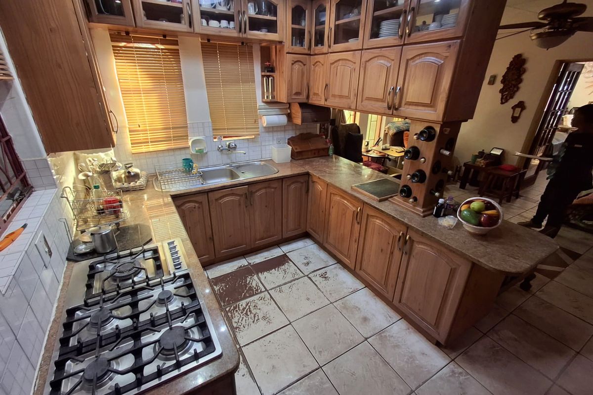 A functional kitchen featuring wooden cabinetry, a gas hob, double sink, and tiled flooring, offering a traditional layout with ample storage space.
