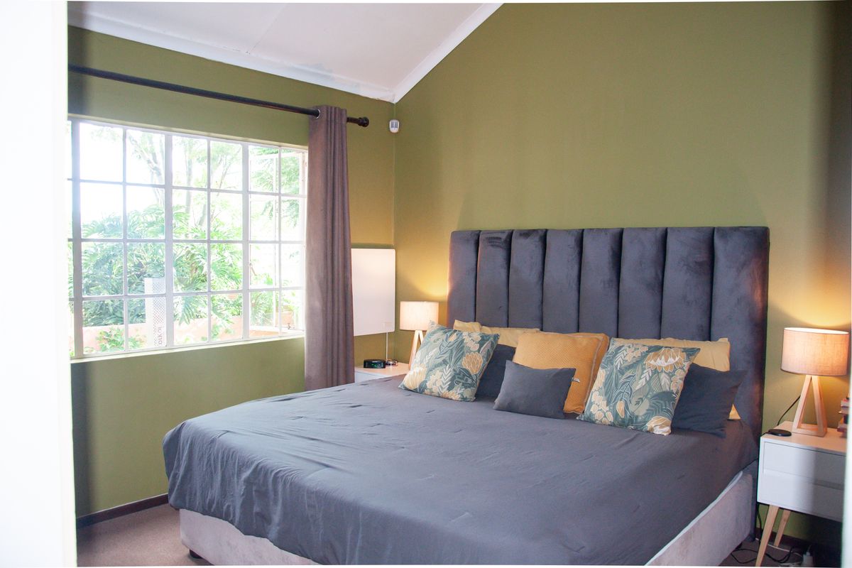A bedroom featuring a vaulted ceiling, large window with natural light, and neutral carpeting.