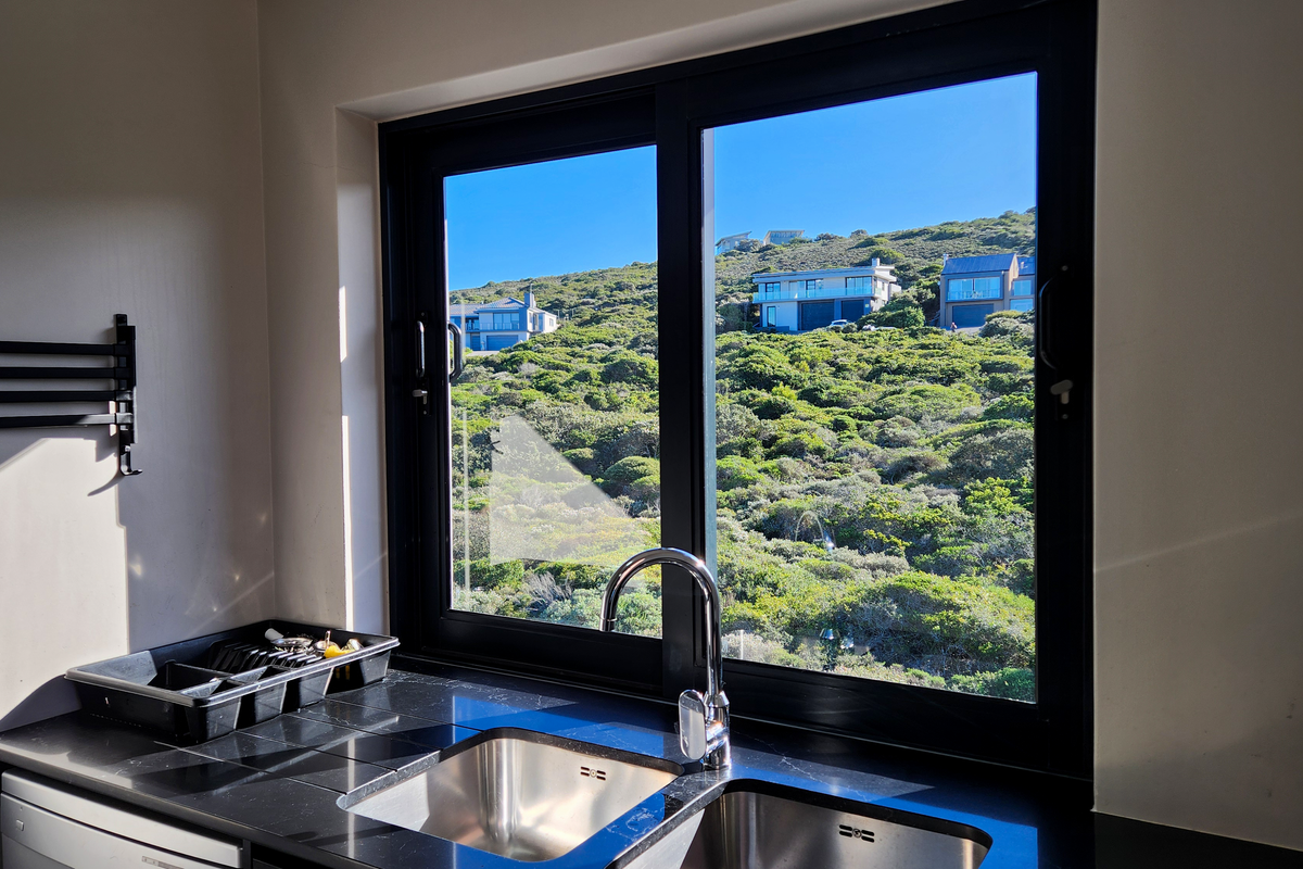 A functional kitchen sink area featuring a modern stainless steel double basin, black tiled countertop, and a large window with scenic hillside views.