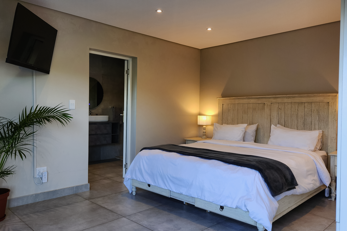A well-maintained bedroom featuring neutral wall tones, large format floor tiles, and an en-suite bathroom access.