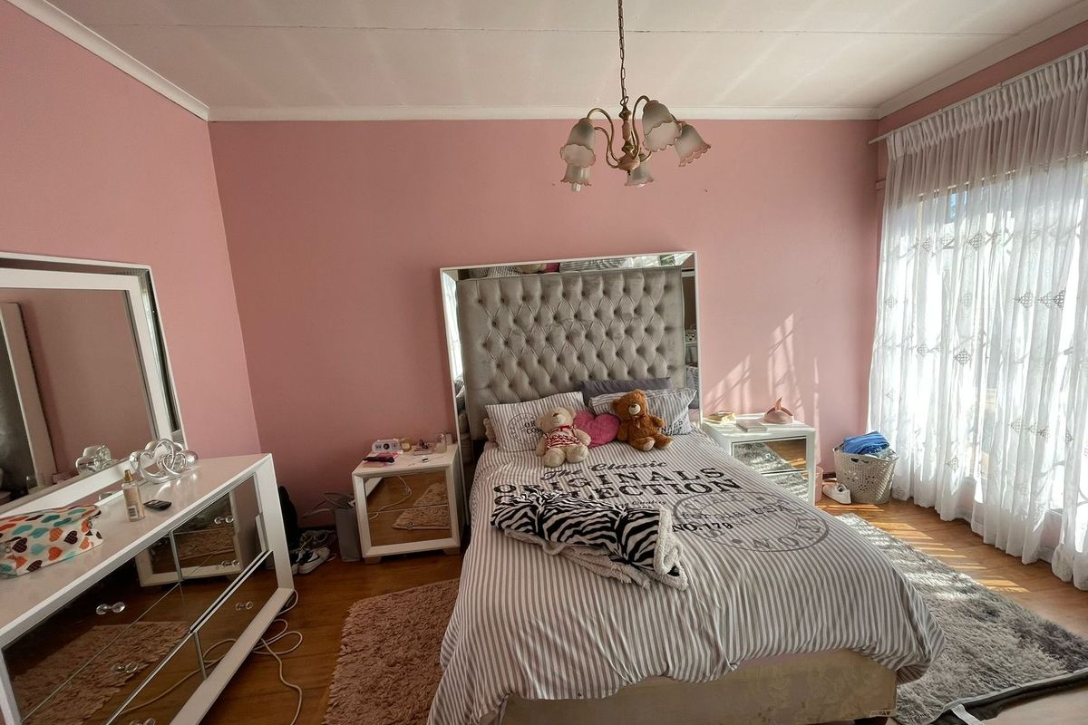 A bedroom featuring pink walls, laminate flooring, and a central light fixture, with natural light entering through a large window.