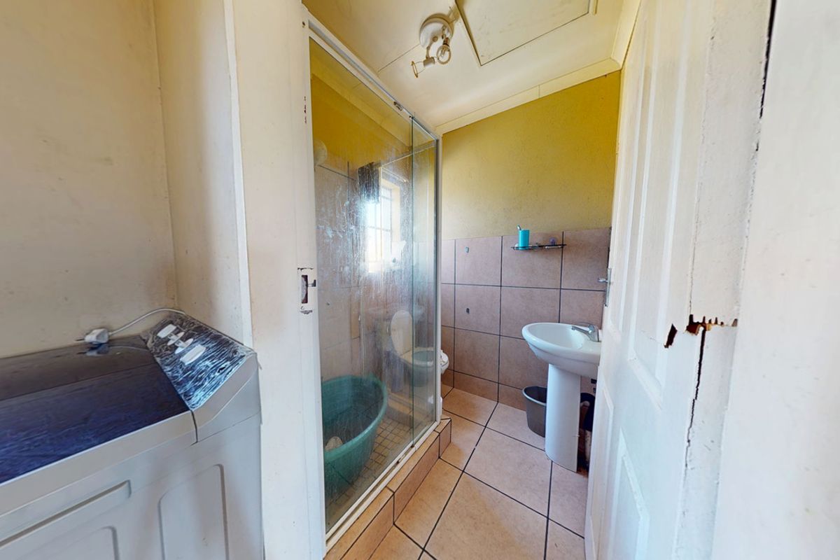 A functional bathroom featuring a shower enclosure, pedestal basin, and toilet, with tiled flooring and wall finishes in need of cosmetic updates.