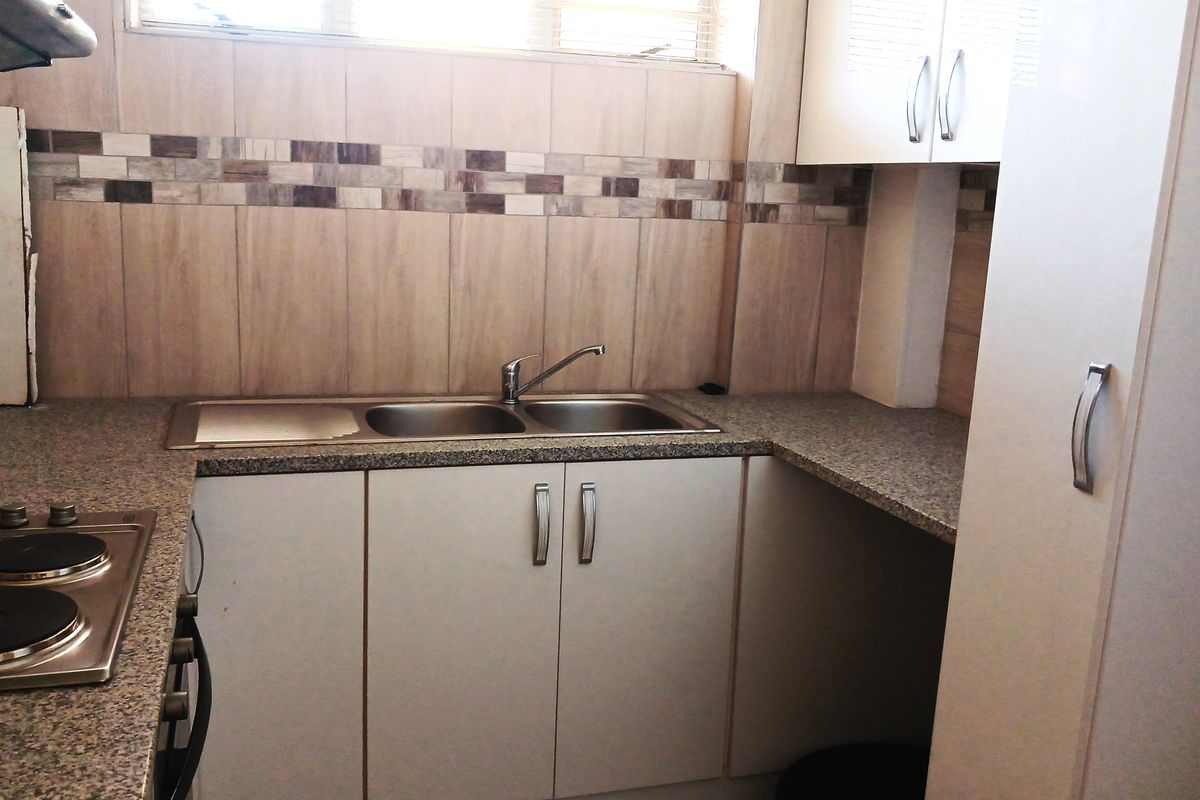 A functional kitchen featuring granite countertops, a double bowl stainless steel sink, built-in cabinetry, and an integrated electric hob with an extractor fan.
