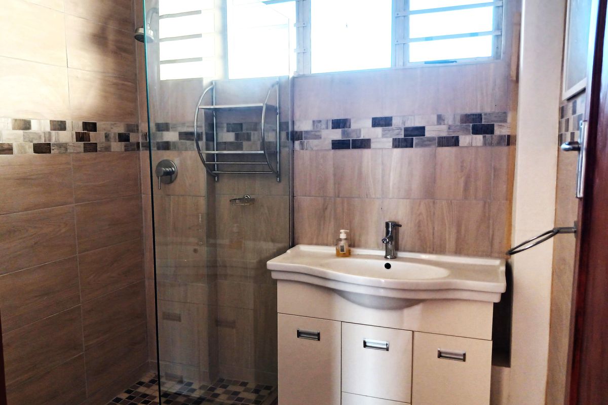 A modern bathroom featuring a glass-enclosed shower, a white vanity cabinet with a basin, and neutral-toned wall tiles with decorative mosaic accents.