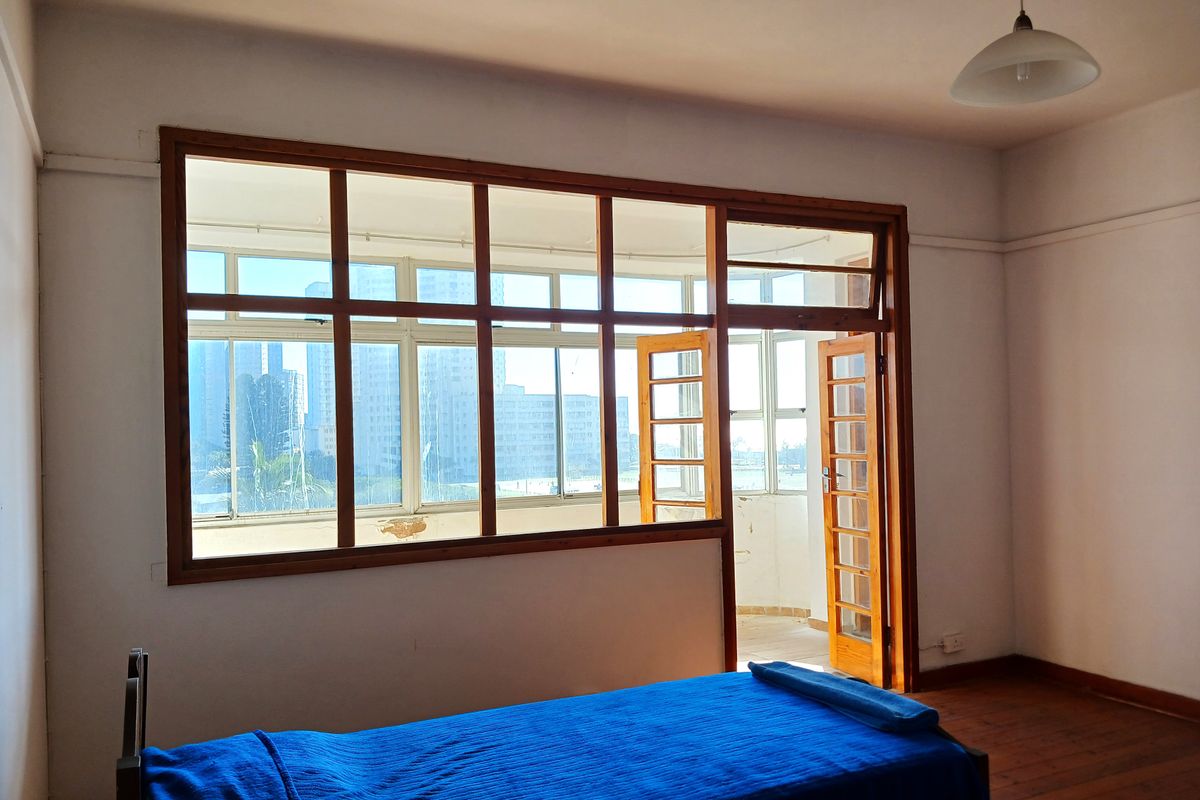 A bedroom featuring hardwood flooring, large wooden-framed windows, and direct access to an enclosed balcony area.