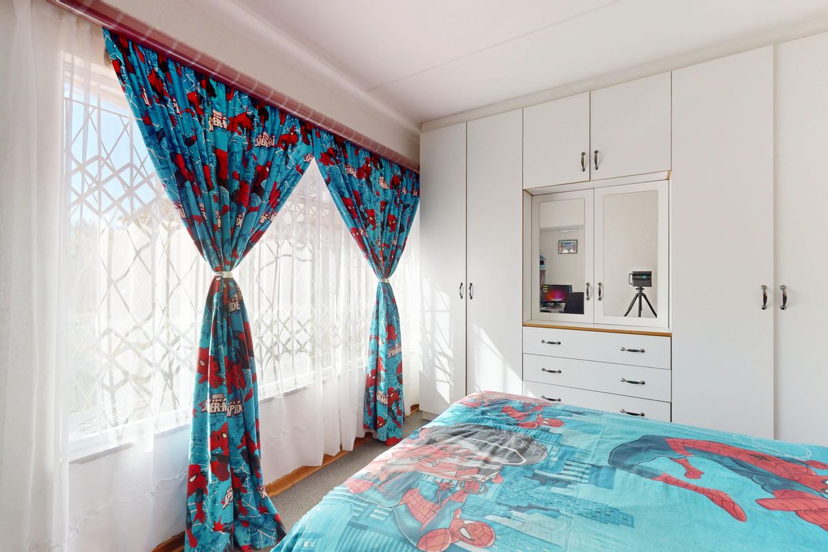 A bedroom featuring white built-in cupboards with integrated drawers and a window fitted with a security gate.