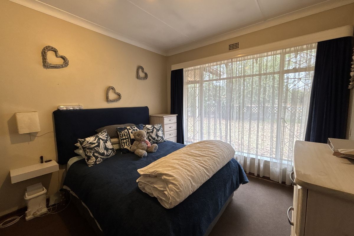 A bedroom featuring a large window with security gate, coving, and neutral wall finishes, offering a functional space with natural light.