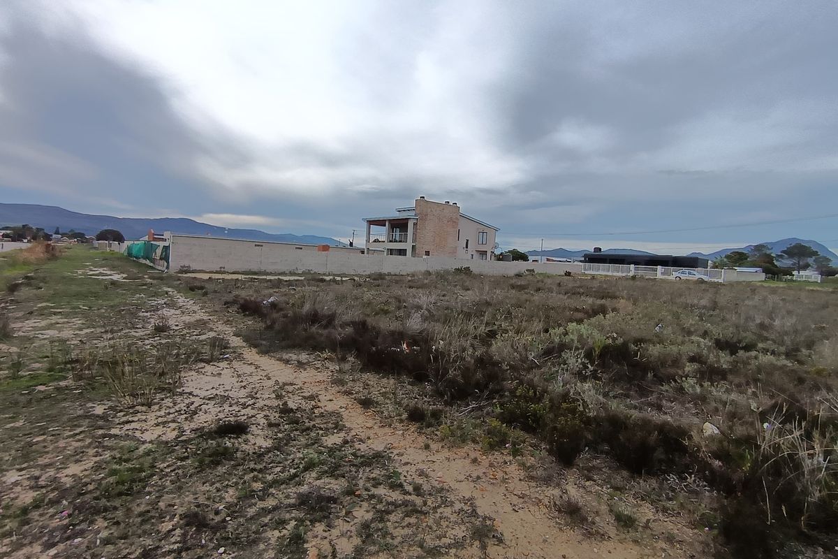 A view of a vacant residential plot featuring natural vegetation and boundary walling, with neighboring properties visible in the background.