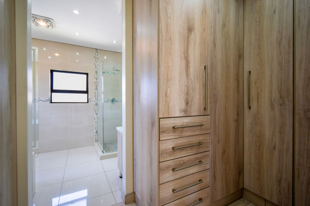 A modern dressing area featuring built-in wood-grain cabinetry, leading into a contemporary bathroom with a glass-enclosed shower and tiled finishes.