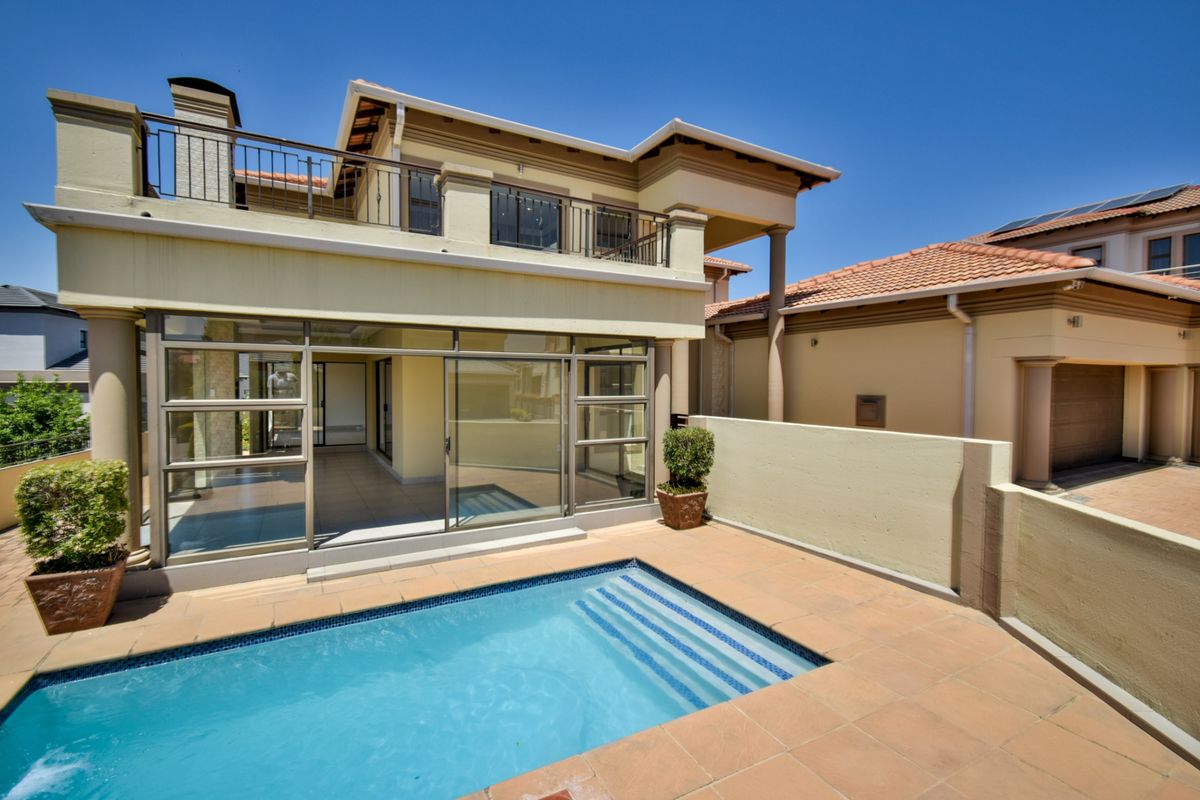Rear view of the property featuring a swimming pool, tiled patio area, and a balcony overlooking the garden.