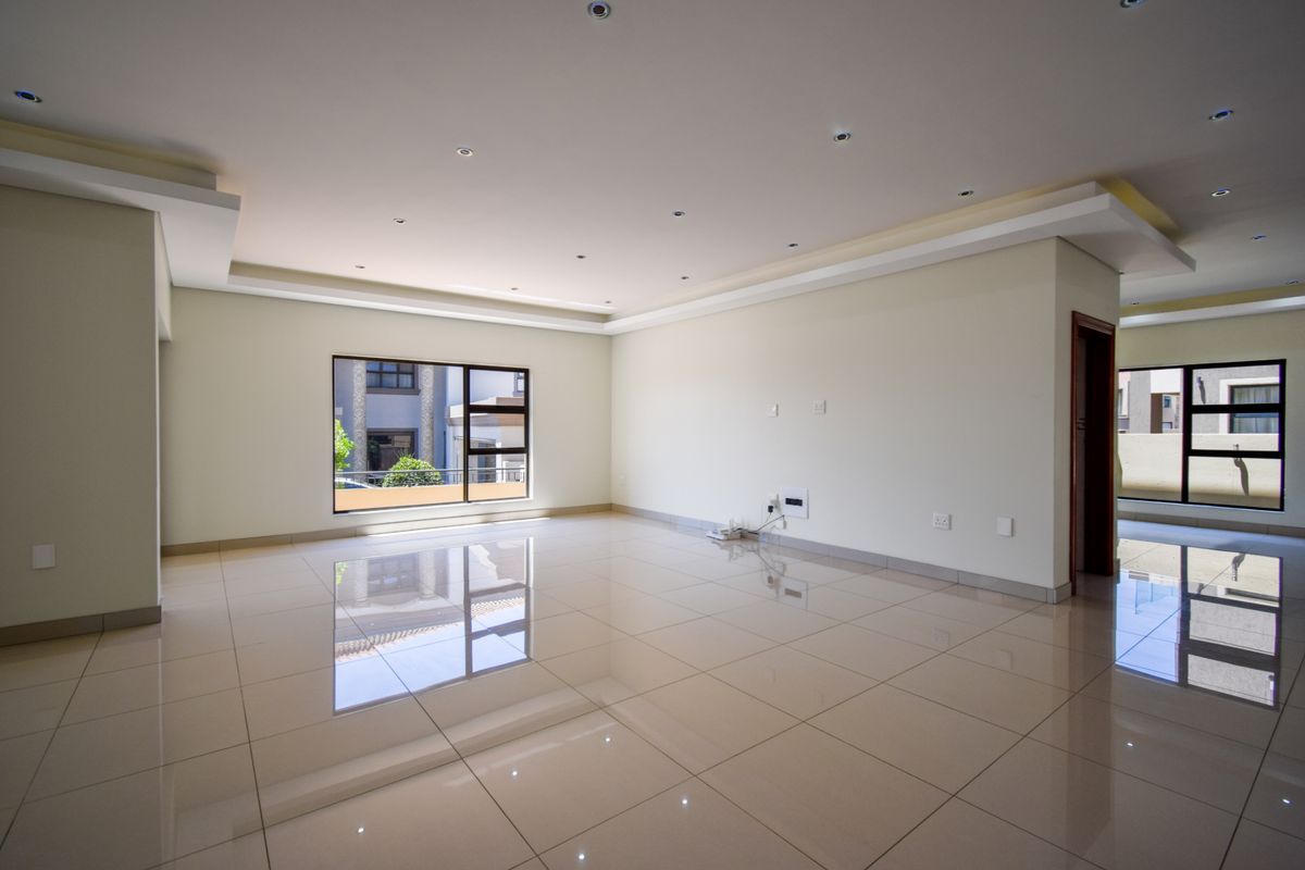A spacious, open-plan living area featuring polished porcelain floor tiles, recessed ceiling lighting, and large windows providing ample natural light.
