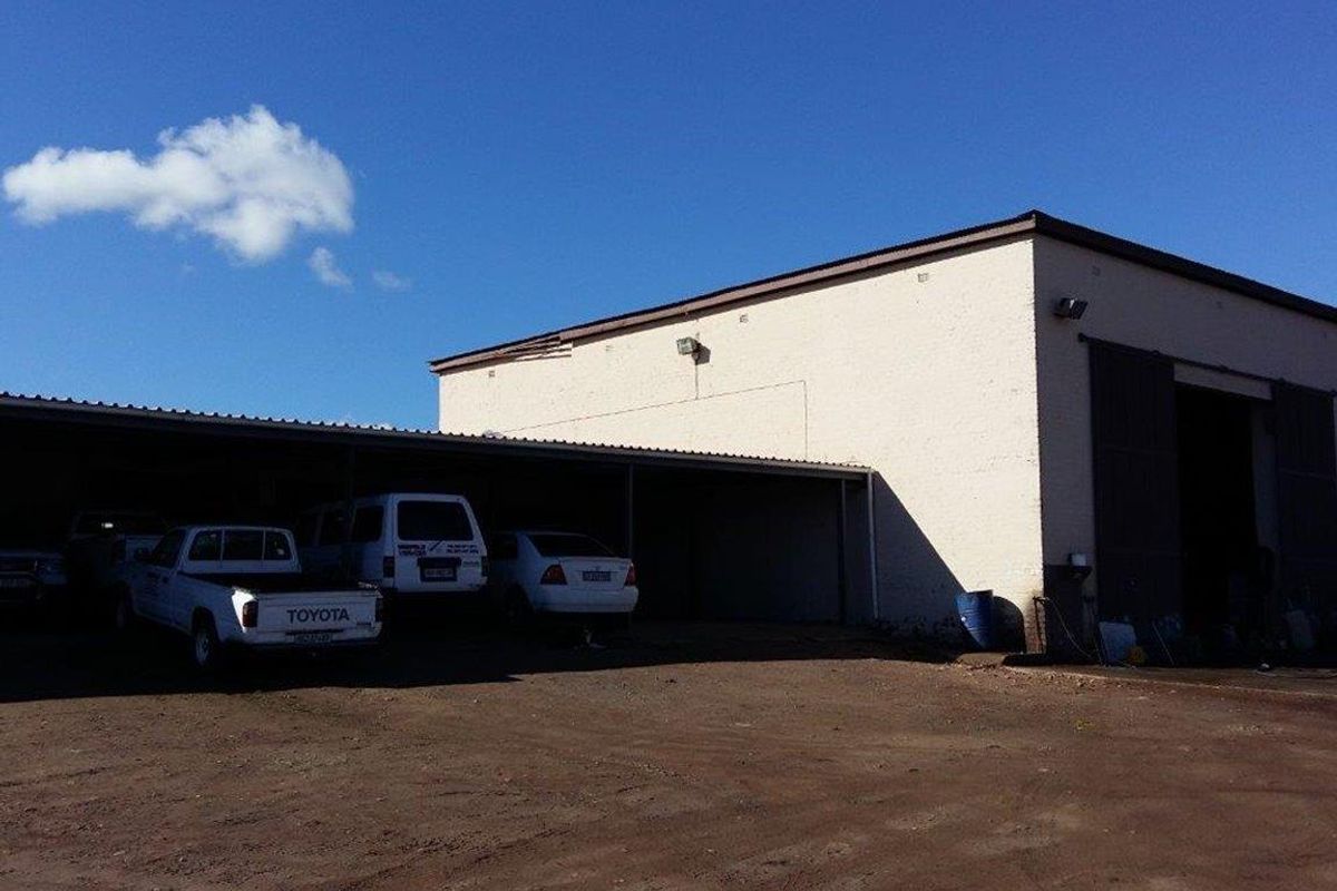 Exterior view of a farm building featuring a large covered parking area and a spacious workshop or storage space with a sliding door.